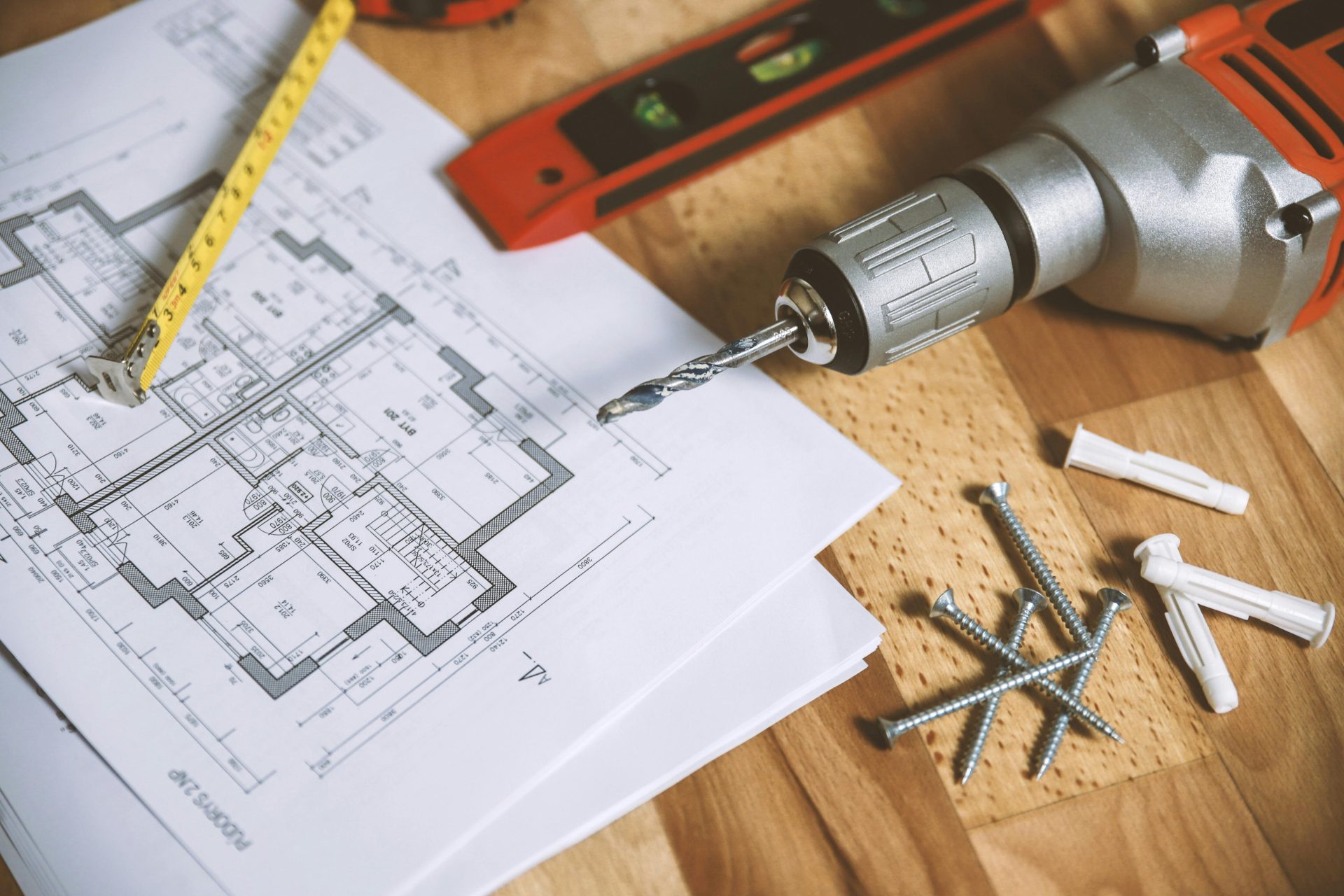Primer plano de un plano de construcción con herramientas como taladro y tornillos sobre una mesa de madera.